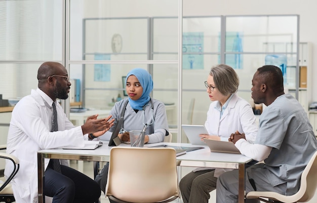 Grupo de médicos sentados à mesa e planejando trabalhar juntos durante reunião no escritório
