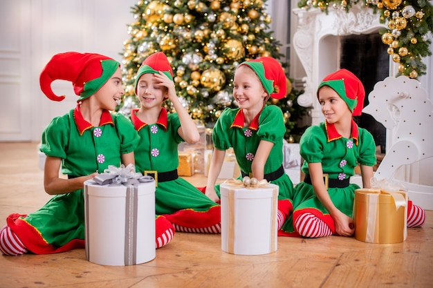 Grupo de meninas-namoradas crianças alegres e felizes em trajes de duendes com presentes no fundo de uma árvore de natal