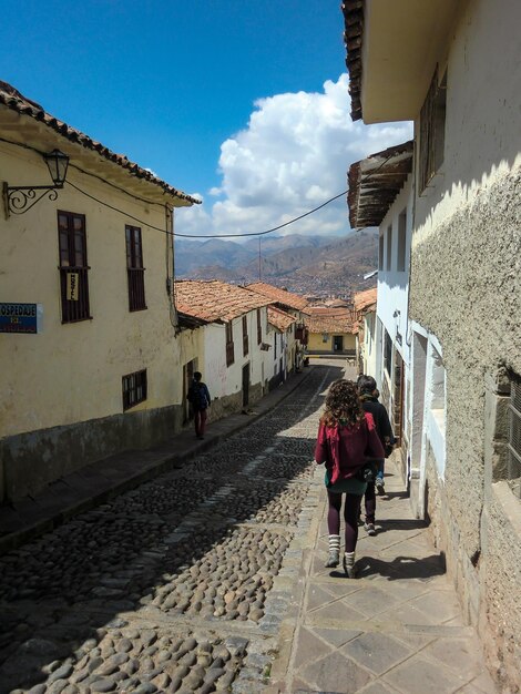 Grupo de mochileiros caminhando ao longo de uma calçada em uma rua estreita de paralelepípedos