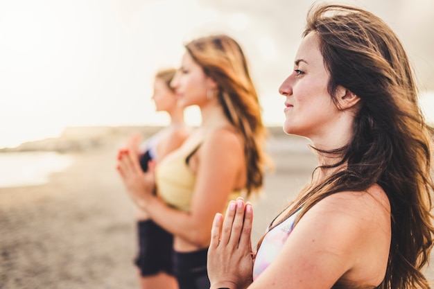 Grupo de mulheres bonitas e saudáveis amigas em meditação de ioga ao ar livre na praia para o conceito de estilo de vida ativo de bem-estar - esporte e pessoas