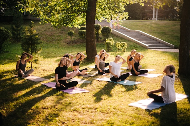 Grupo de mulheres esticando o pescoço no parque da cidade em uma manhã ensolarada de verão sob a orientação do instrutor