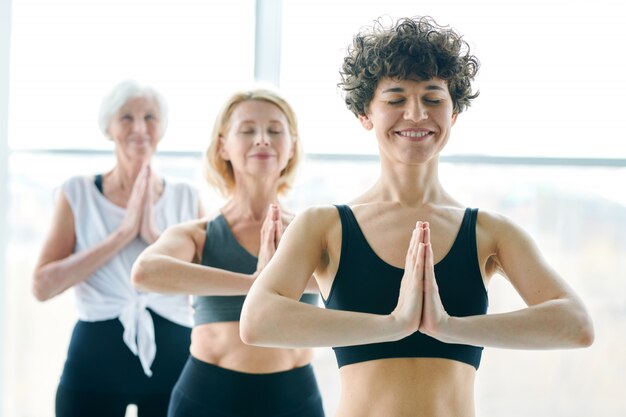 Grupo de mulheres fazendo ioga e meditando ao lado de uma grande janela