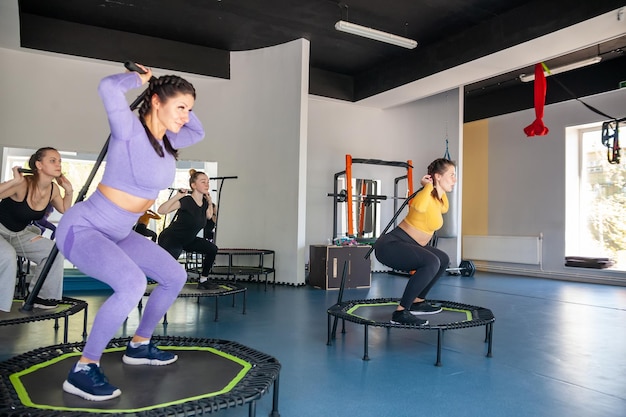 Grupo de mulheres felizes aquecendo antes do treino no ginásio pulando no trampolim