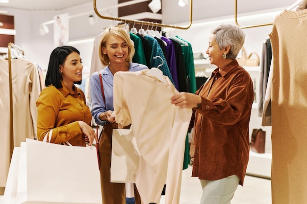 Grupo de mulheres felizes comprando roupas em boutique e procurando blusas