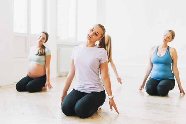 Grupo de mulheres grávidas em uniformes esportivos com treinador fazendo ginástica no estúdio brilhante