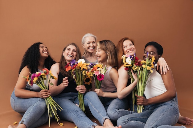 Grupo de mulheres multiétnicas sentadas juntas em um estúdio seis fêmeas sorridente com buquês