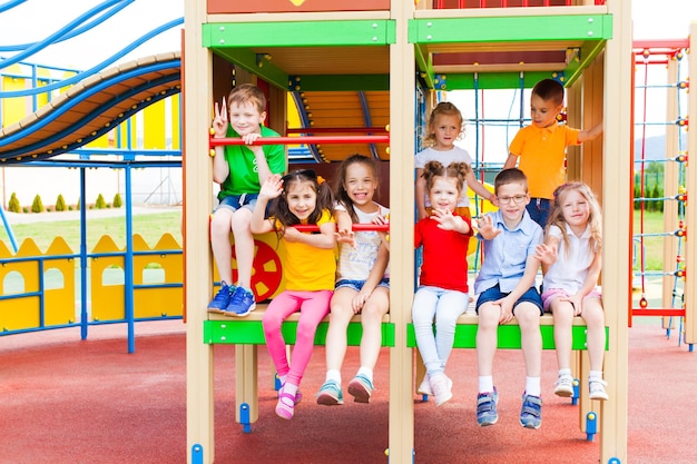 Grupo de oito pré-escolares alegres sentados juntos no quadro de escalada dentro da construção no playground ao ar livre no parque de verão