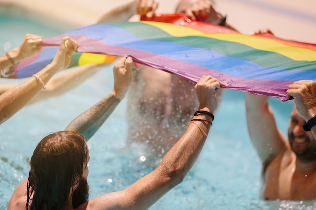 Grupo de pessoas acenando uma bandeira lgtb dentro de uma piscina