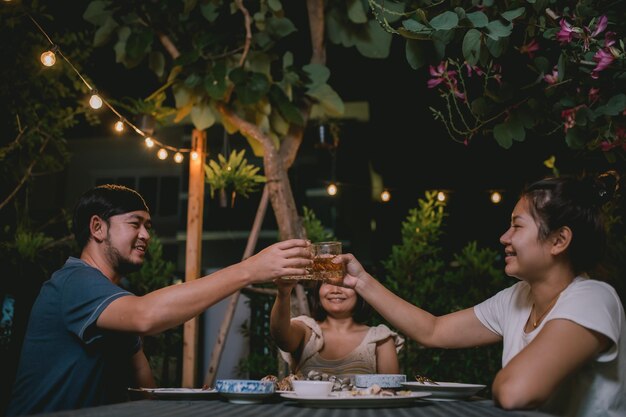 Grupo de pessoas asiáticas jantando festa no jardim de casa de fériasCelebração da festa no jardim da noite de verão com amigos