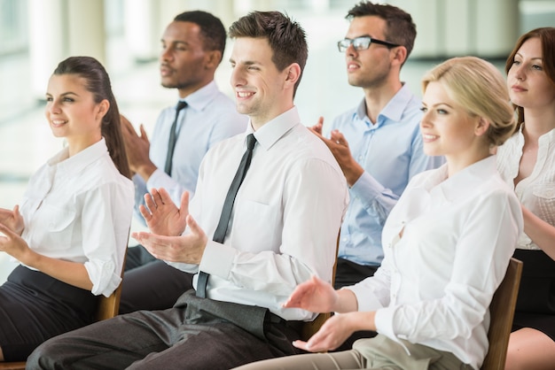 Grupo de pessoas batendo palmas de mãos durante uma conferência de reunião.