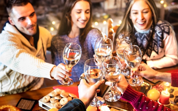 Grupo de pessoas comemorando o Natal brindando com champanhe em um jantar caseiro - Foco nos copos