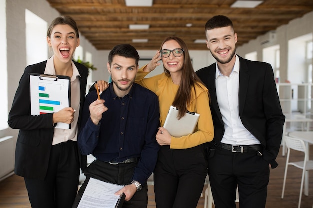 Foto grupo de pessoas criativas alegres em ternos olhando alegremente para a câmera juntos enquanto passam tempo no escritório moderno