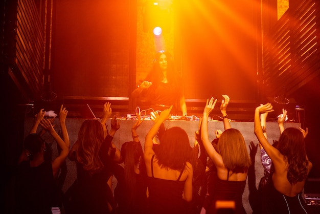 Grupo de pessoas dançando na discoteca ao som da música do dj no palco