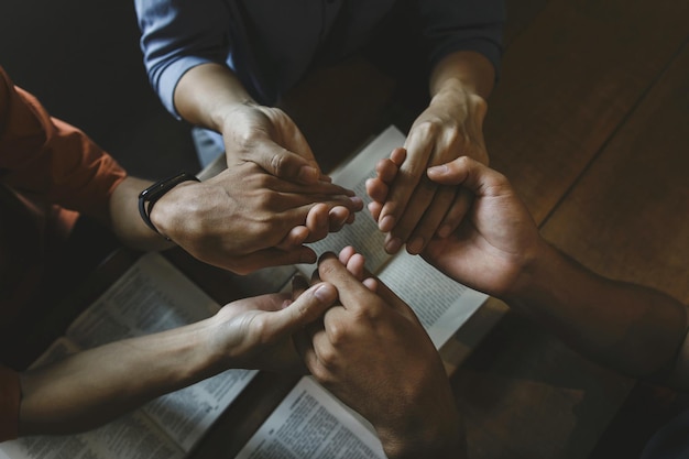 Grupo de pessoas de mãos dadas orando adoração acredita com a bíblia em uma mesa de madeira