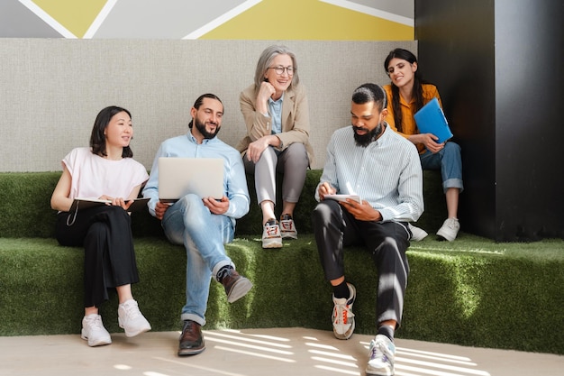 Grupo de pessoas de negócios diversas a realizar uma reunião informal usando um portátil e a fazer anotações no escritório