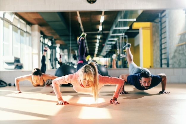 Grupo de pessoas desportivos com hábitos saudáveis, fazendo exercícios de força no chão do ginásio. no espelho de fundo.