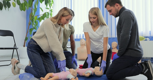 Grupo de pessoas durante o treinamento de primeiros socorros com instrutor mostrando no manequim como fazer respiração artificial para o bebê.