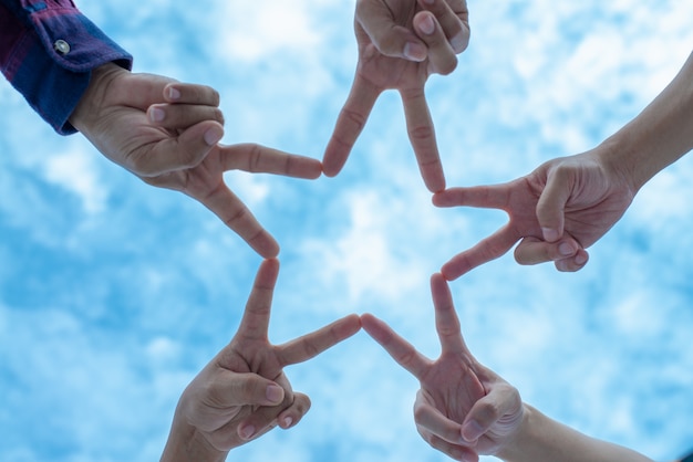 Grupo de pessoas em cinco pessoas usando os dedos para fazer a forma de estrela com céu azul.