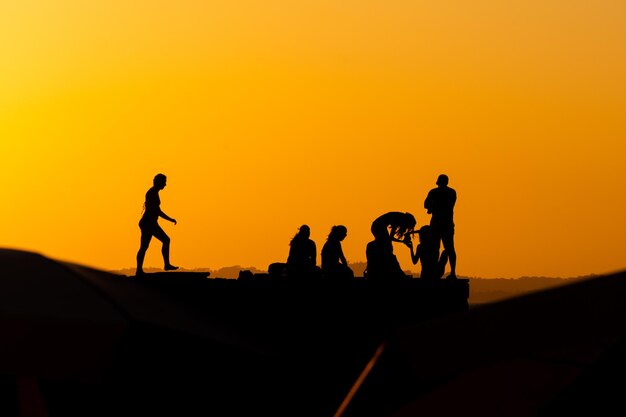 Grupo de pessoas em silhueta são vistas no cais de Porto da Barra contra o pôr-do-sol na cidade de Salvador Bahia