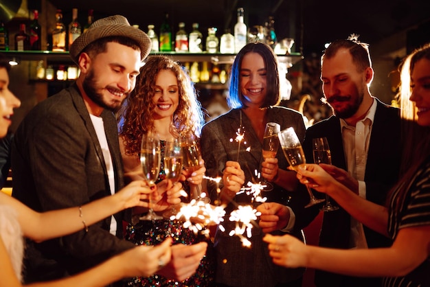 Grupo de pessoas felizes segurando estrelinhas na festa. Jovens amigos tilintando taças de champanhe.