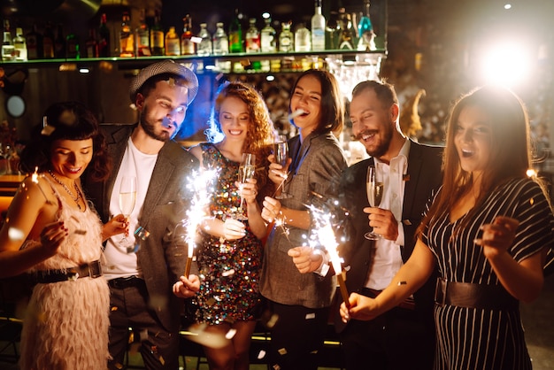 Grupo de pessoas felizes segurando estrelinhas na festa. Jovens amigos tilintando taças de champanhe.