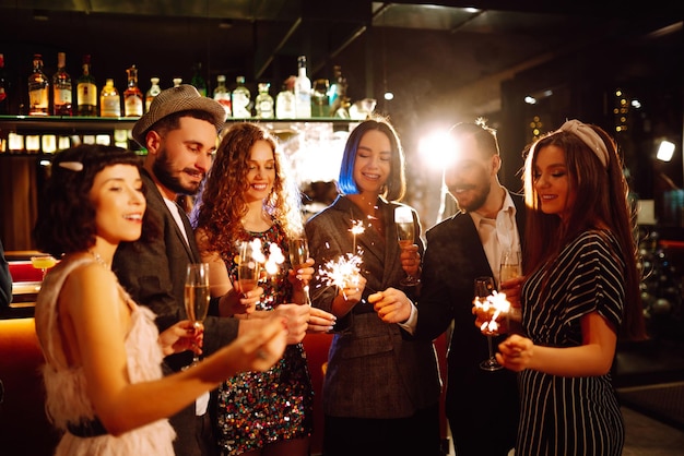 Grupo de pessoas felizes segurando estrelinhas na festa. Jovens amigos tilintando taças de champanhe.