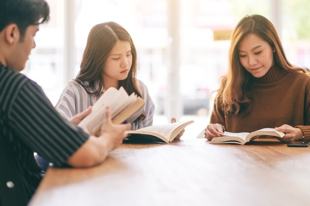 Grupo de pessoas sentadas e lendo um livro juntos na mesa de madeira