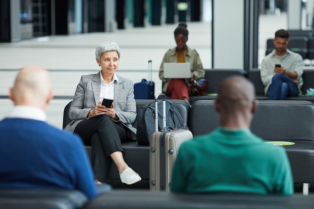 Grupo de pessoas sentadas na sala de espera e esperando o voo no aeroporto