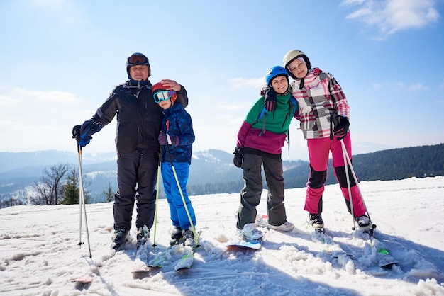 Grupo de pessoas sorridentes em esquis e snowboard na neve profunda no fundo do céu azul e montanhas.