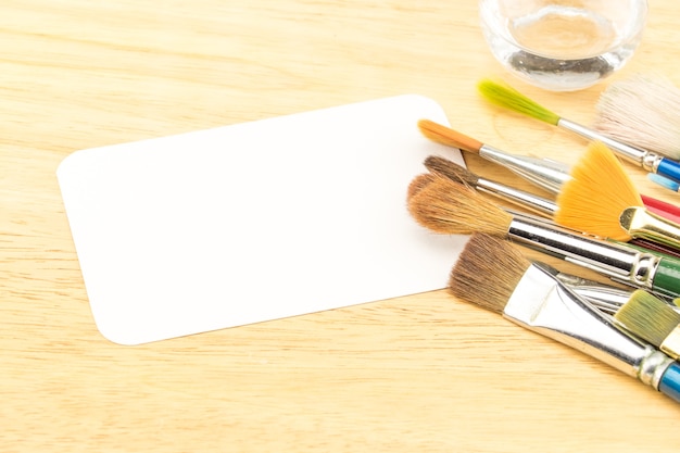 Grupo de pincel aquarela e cartão de papel branco em branco na mesa de madeira
