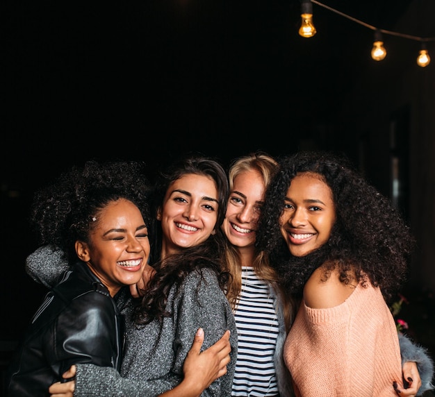 Grupo de quatro amigas rindo abraçando-se à noite