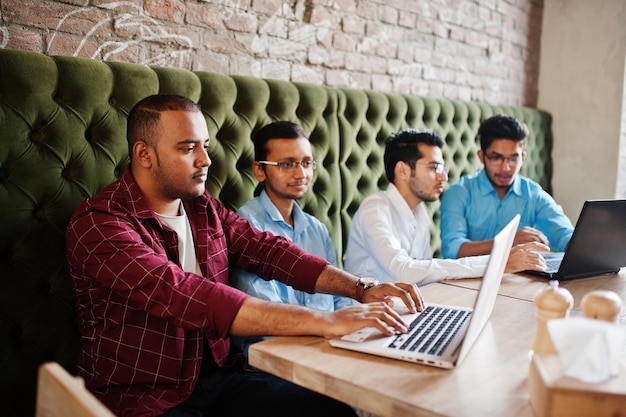 Grupo de quatro homens do sul da Ásia posaram em reunião de negócios no café índios trabalham com laptops juntos usando vários gadgets conversando