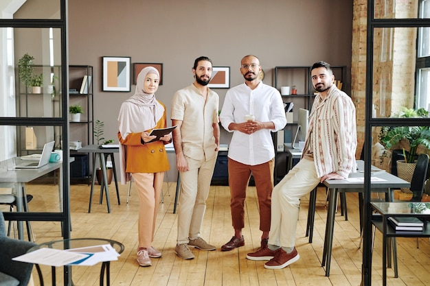 Grupo de quatro jovens funcionários bem sucedidos em roupas casuais em pé no escritório