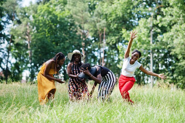 Grupo de quatro lindas mulheres afro-americanas usam chapéu de verão pulando na grama verde no parque