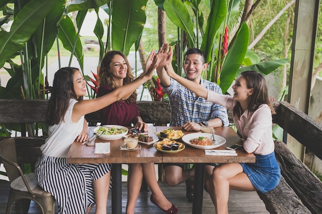 Grupo de quatro melhores amigos fazendo high five enquanto almoçam juntos em um café