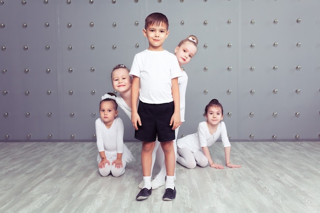 Grupo de quatro pequenas bailarinas e bailarino infantil posando juntos e praticando