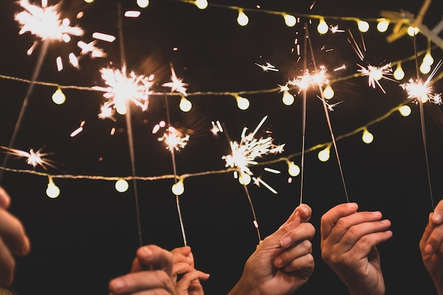 Grupo de quatro pessoas curtindo a noite de ano novo, comemorando com fogos de artifício no meio e olhando para a câmera - adultos se divertindo juntos