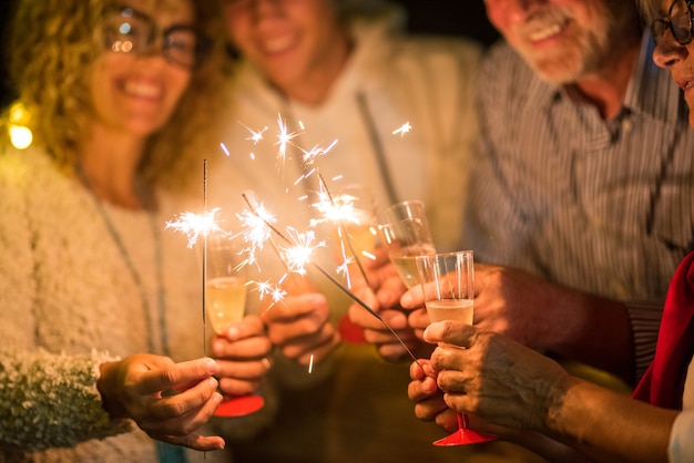 Grupo de quatro pessoas se divertindo e segurando taças de champanhe e espumantes comemorando o feliz ano novo juntos