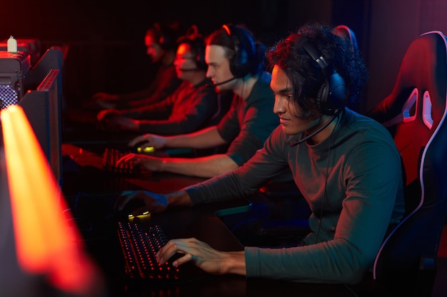 Grupo de rapazes com fones de ouvido, sentados à mesa na frente de computadores e jogando no clube de computador