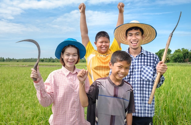 Grupo de rir homem feliz agricultor asiático, mulher e dois filhos sorriam e segurando ferramentas no campo de arroz verde