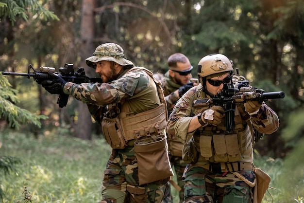 Grupo de soldados armados atentos em trajes de camuflagem movendo-se com rifles na floresta enquanto trabalham na operação de limpeza