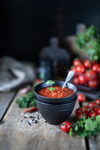 Grupo de tomate cereja vermelho como um ingrediente para o molho de tomate em uma tigela preta em uma mesa de madeira.