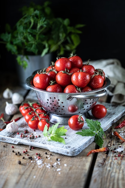 Grupo de tomates de cereja vermelhos em uma peneira do metal em uma tabela de madeira.