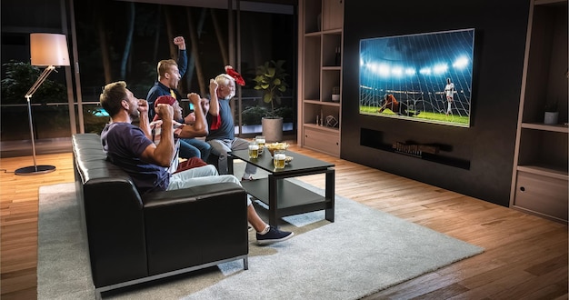 Grupo de torcedores assiste a um momento de futebol na TV e comemora um gol sentados no sofá da sala A sala é feita em 3D