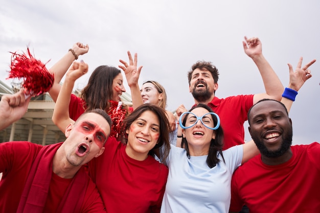 Grupo de torcedores de um time de futebol nas arquibancadas vestindo camisetas vermelhas com um torcedor do time adversário