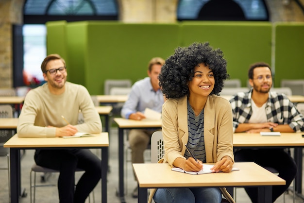 Grupo de treinamento da equipe do projeto de jovens multirraciais felizes sentados em mesas no moderno