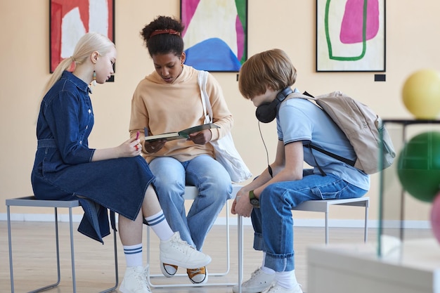 Grupo de três adolescentes sentados em círculo fazendo projeto escolar na galeria de arte