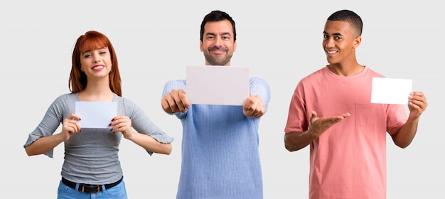 Grupo de três amigos, segurando um cartaz branco vazio para inserir