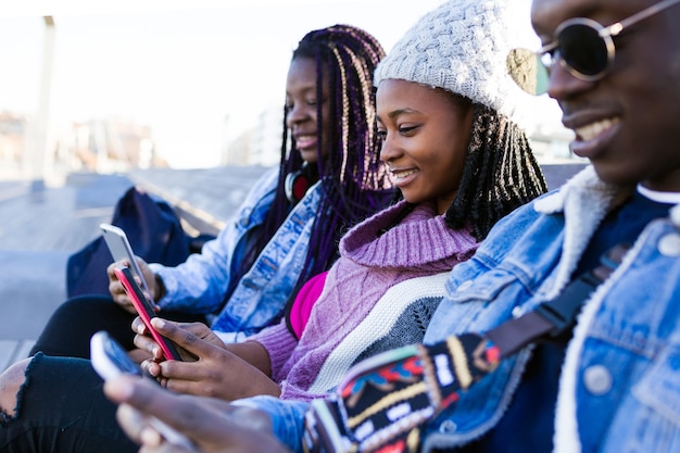 Grupo de três amigos usando o telefone celular na rua.