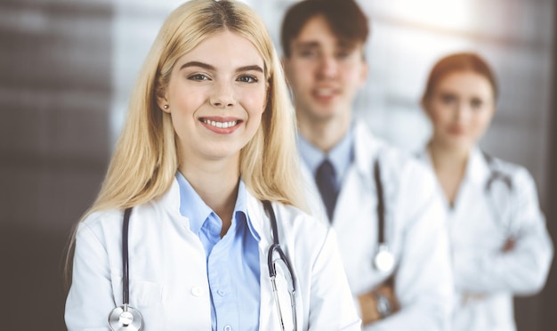 Grupo de três jovens médicos de pé como uma equipe com os braços cruzados em uma clínica moderna e prontos para ajudar os pacientes.